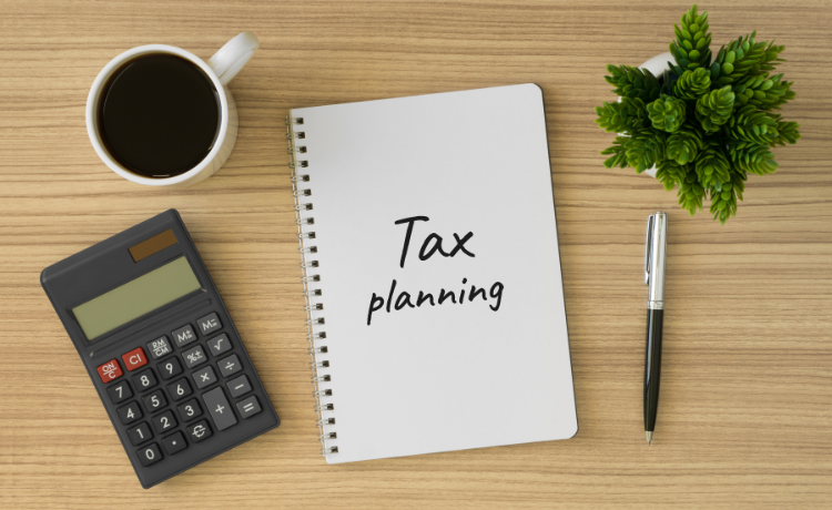 A desk with a coffee, calculator, pen, succulent, and white notebook with "Tax planning" written on the front